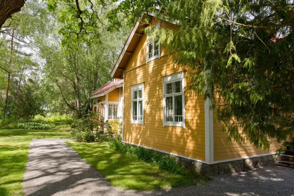 Keltainen puutalo ja hoidettu piha kesäisenä päivänä