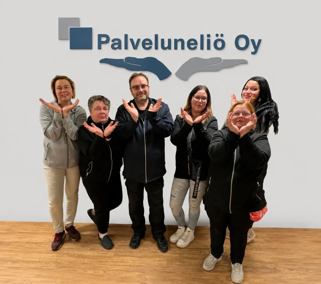 Kuusi Palveluneliön työntekijää seisoo yrityksen logon edessä kädet neliön muotoon aseteltuina